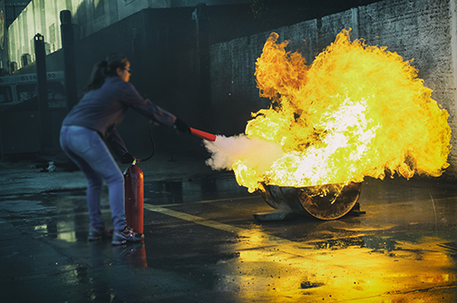 Woman Wearing Goggles Putting out Large Fire With an Extinguisher